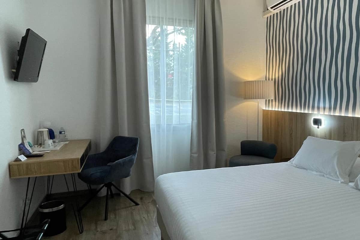 A hotel room with a bed, a desk, a chair, a TV, and a window with curtains.