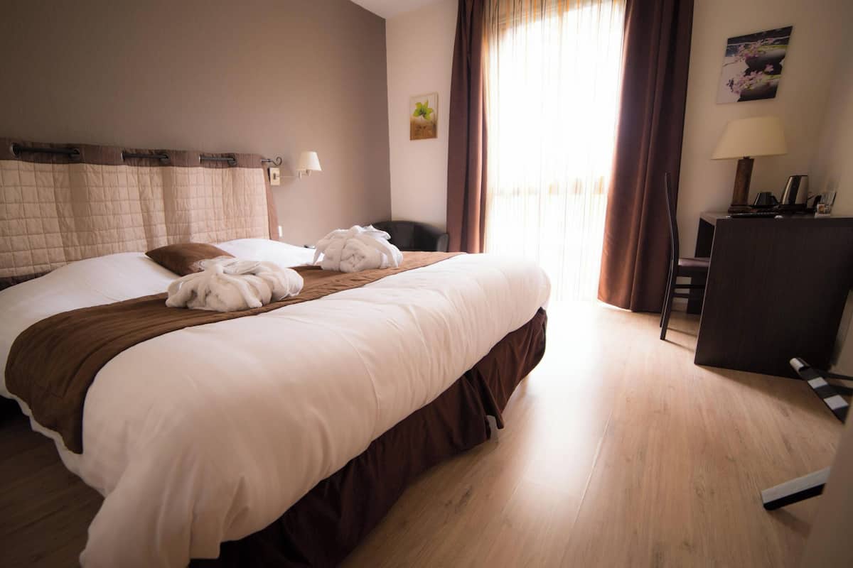 A hotel room with a large bed, a desk, and a chair.