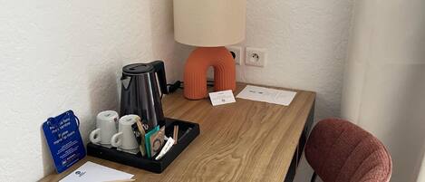 A hotel room with a wooden desk, a coffee maker, a lamp, and a chair.