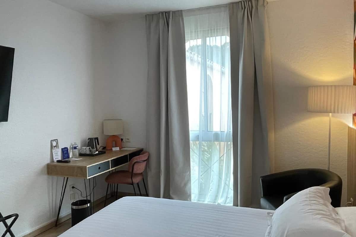 A hotel room with a bed, desk, chair, and a TV mounted on the wall.