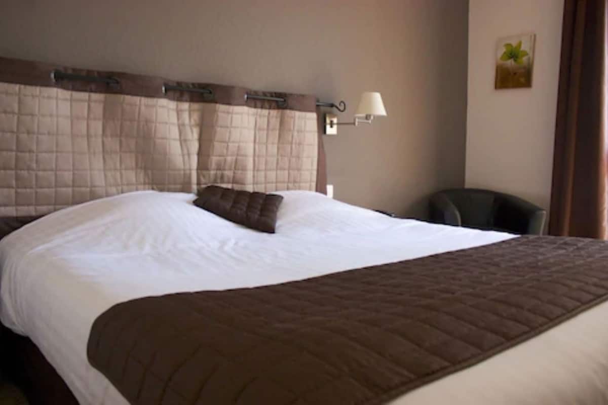 A hotel room with a large bed, a bedside lamp, a chair, and a wall-mounted picture.