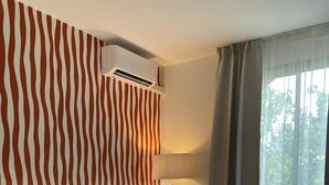 A hotel room with a large bed, a red chair, a wall-mounted air conditioner, and a view of greenery through the window. - Best Western Le Clos de l'Aube Rouge (Castelnau-le-Lez)