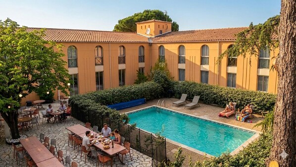 Un patio con piscina, mobiliario exterior y un edificio con varias ventanas.