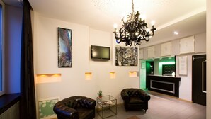 A modern living room with two leather sofas, a flat-screen TV, a chandelier, and a reception desk with a green-lit area. - Hôtel Esplanade (Strasbourg)