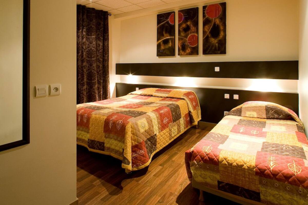 A hotel room with two beds, a wooden floor, a ceiling with a grid pattern, and artwork on the wall.