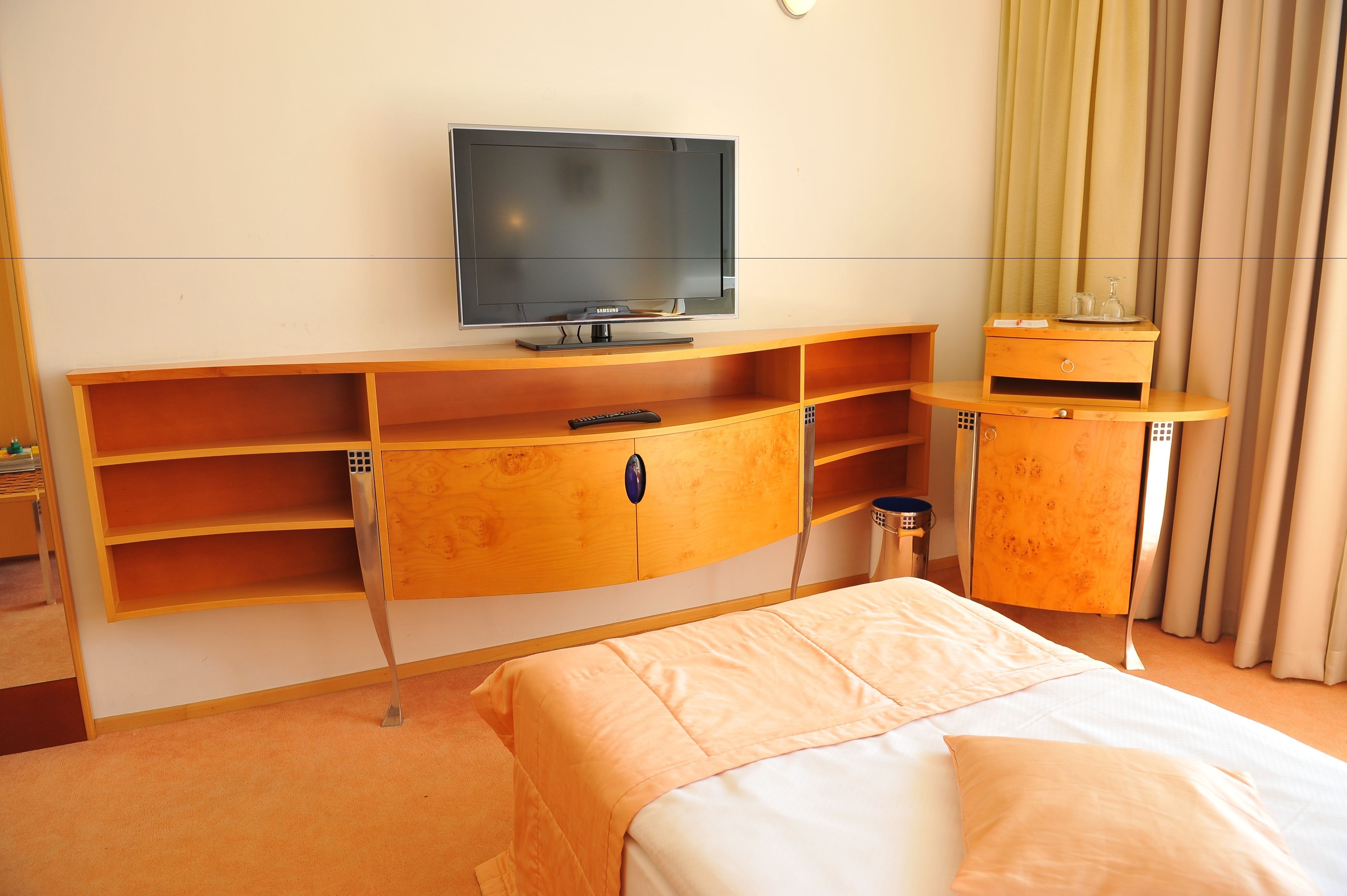 Habitación de hotel con una cama, un televisor sobre un soporte de madera, un armario pequeño y un espejo.