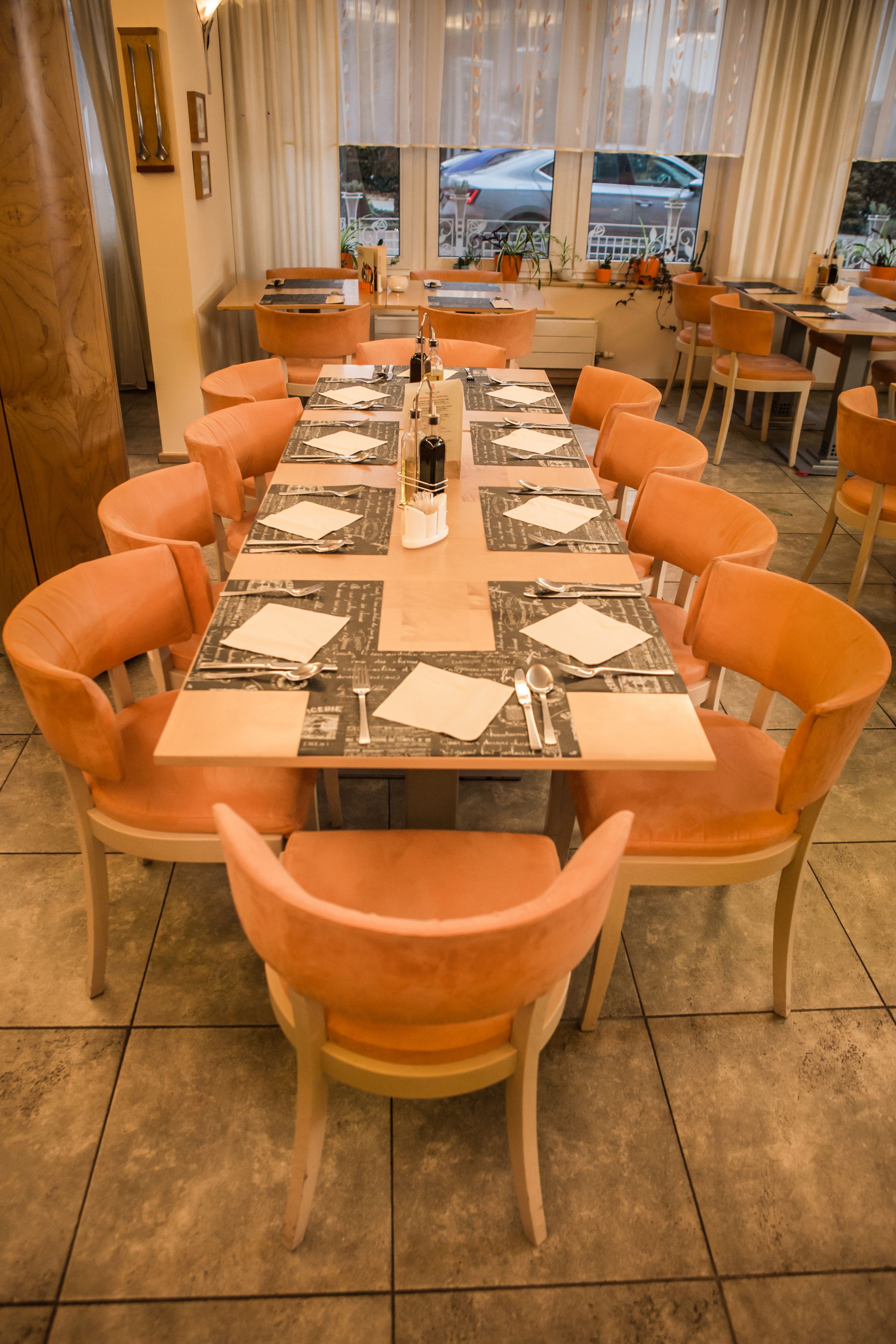 Un comedor con una larga mesa dispuesta para varias personas, rodeada de sillas color naranja.