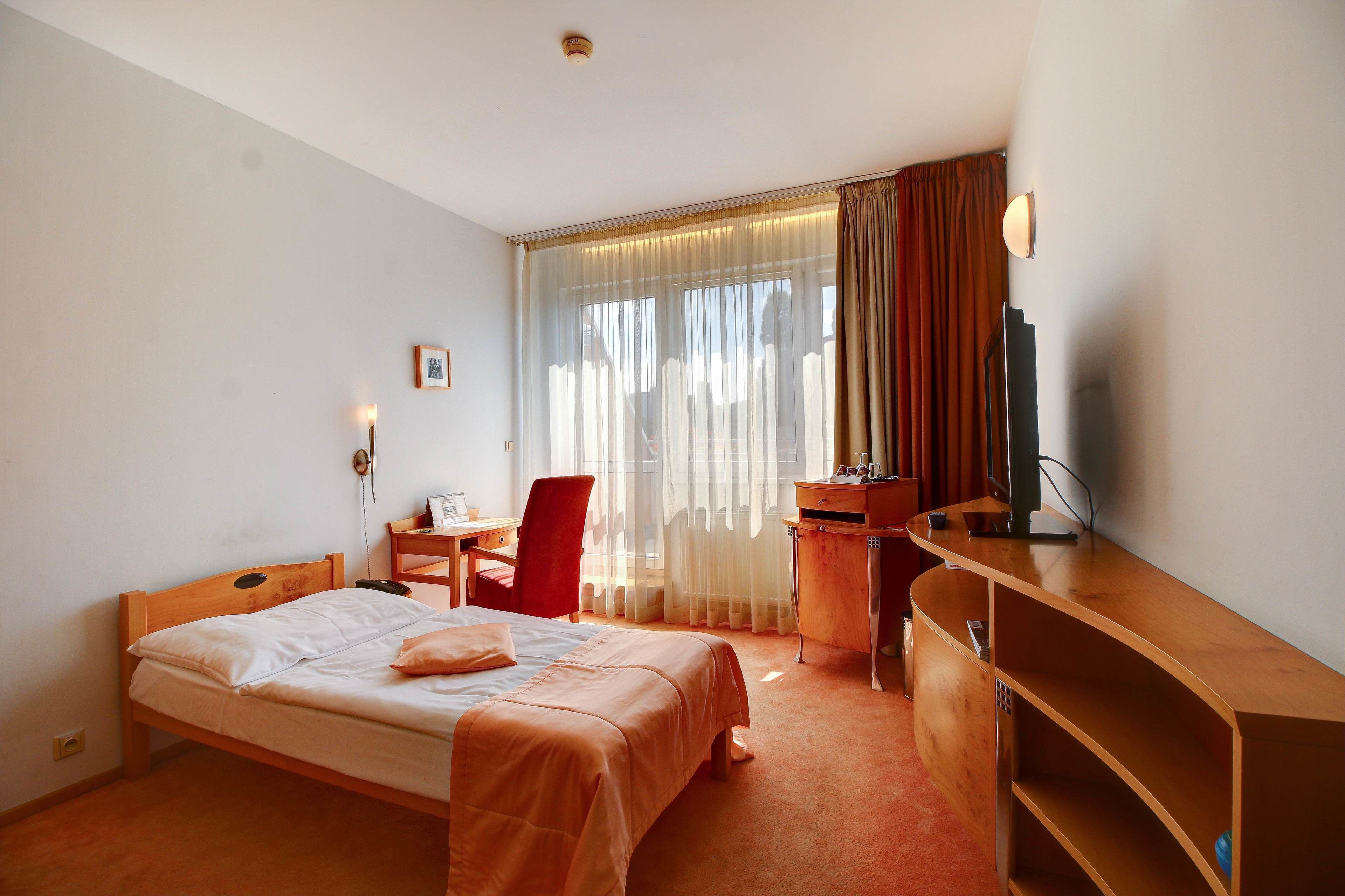 Une chambre d’hôtel avec un lit, un bureau, une chaise, une télévision et une fenêtre avec des rideaux.