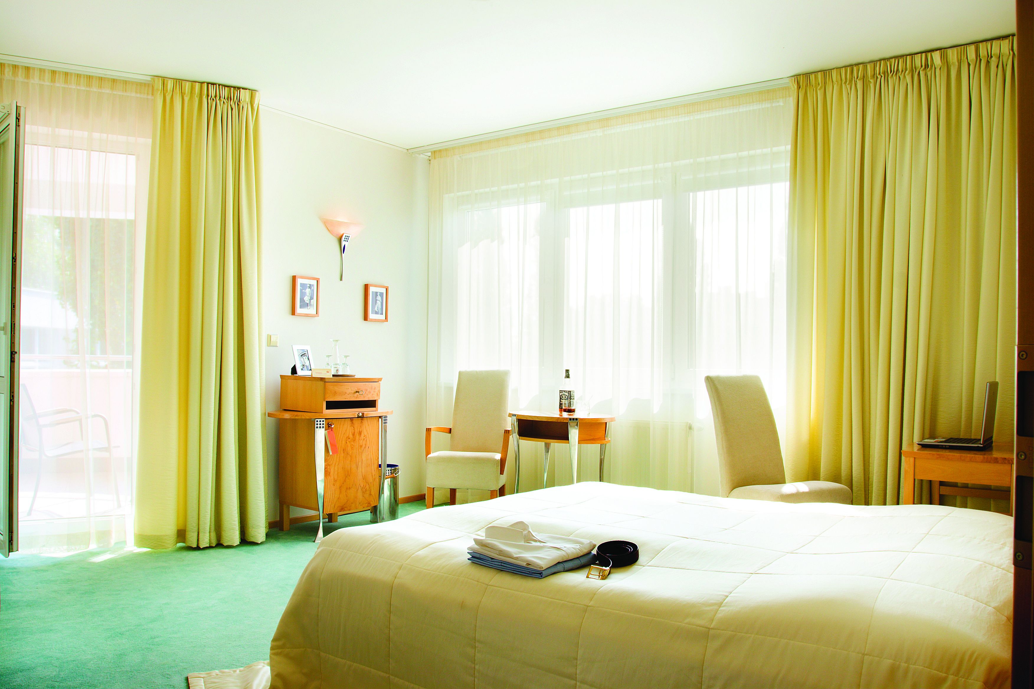 A hotel room with a bed, a desk, two chairs, a lamp, and a window with curtains.