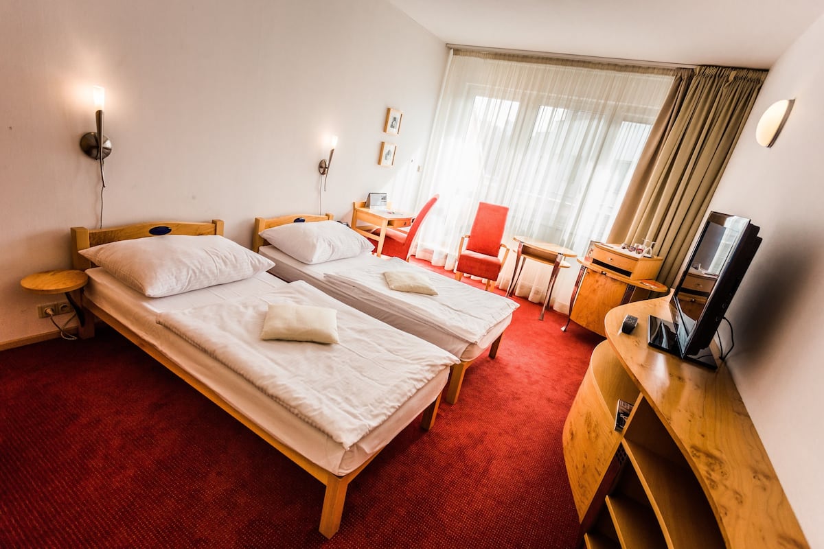 A hotel room with two single beds, a desk, a chair, a TV, and a window with curtains.