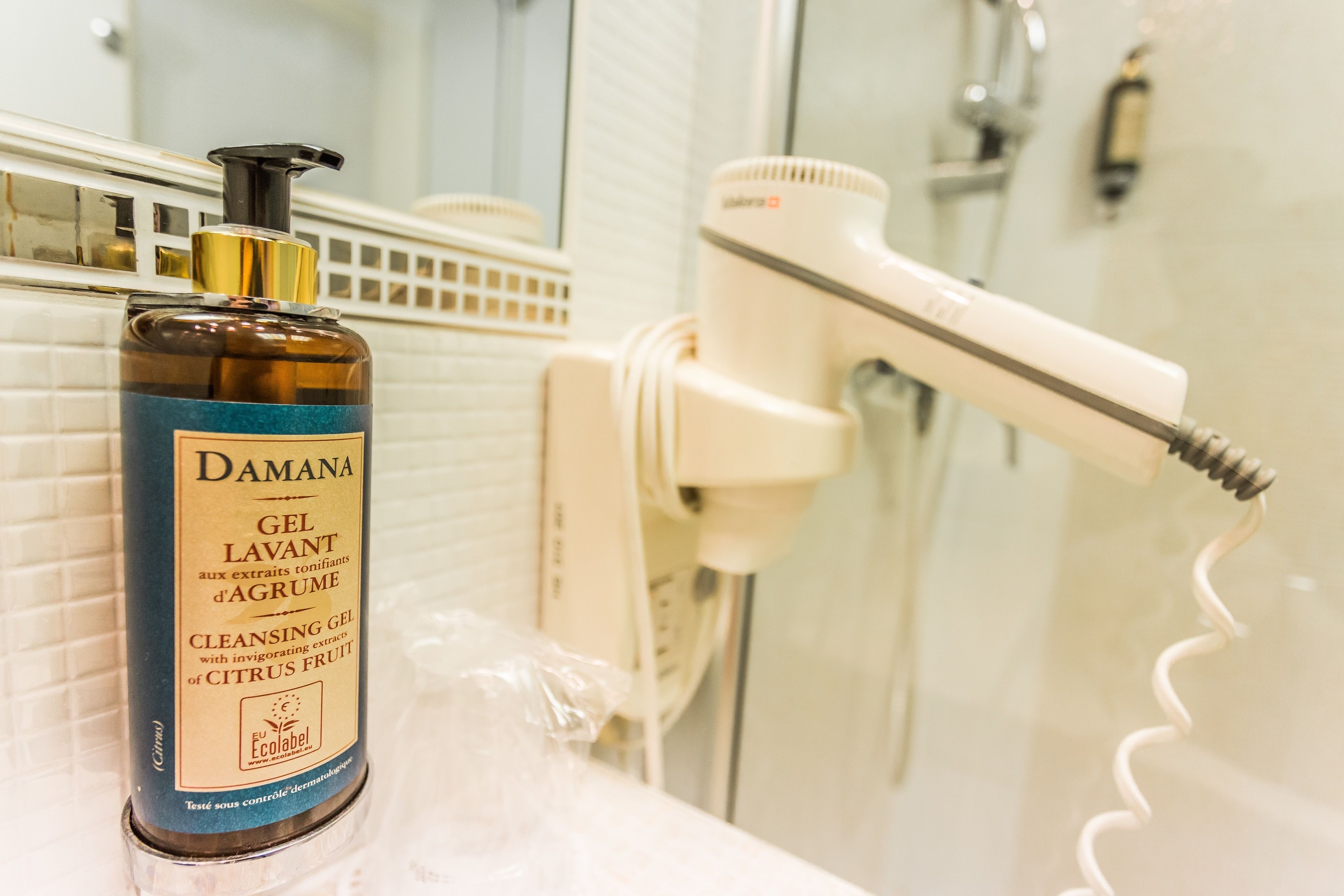 A bathroom with a bottle of Damana cleansing gel, a hairdryer, and a shower area.