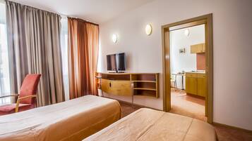 A hotel room with two beds, a TV, a desk, and a view of the kitchen.