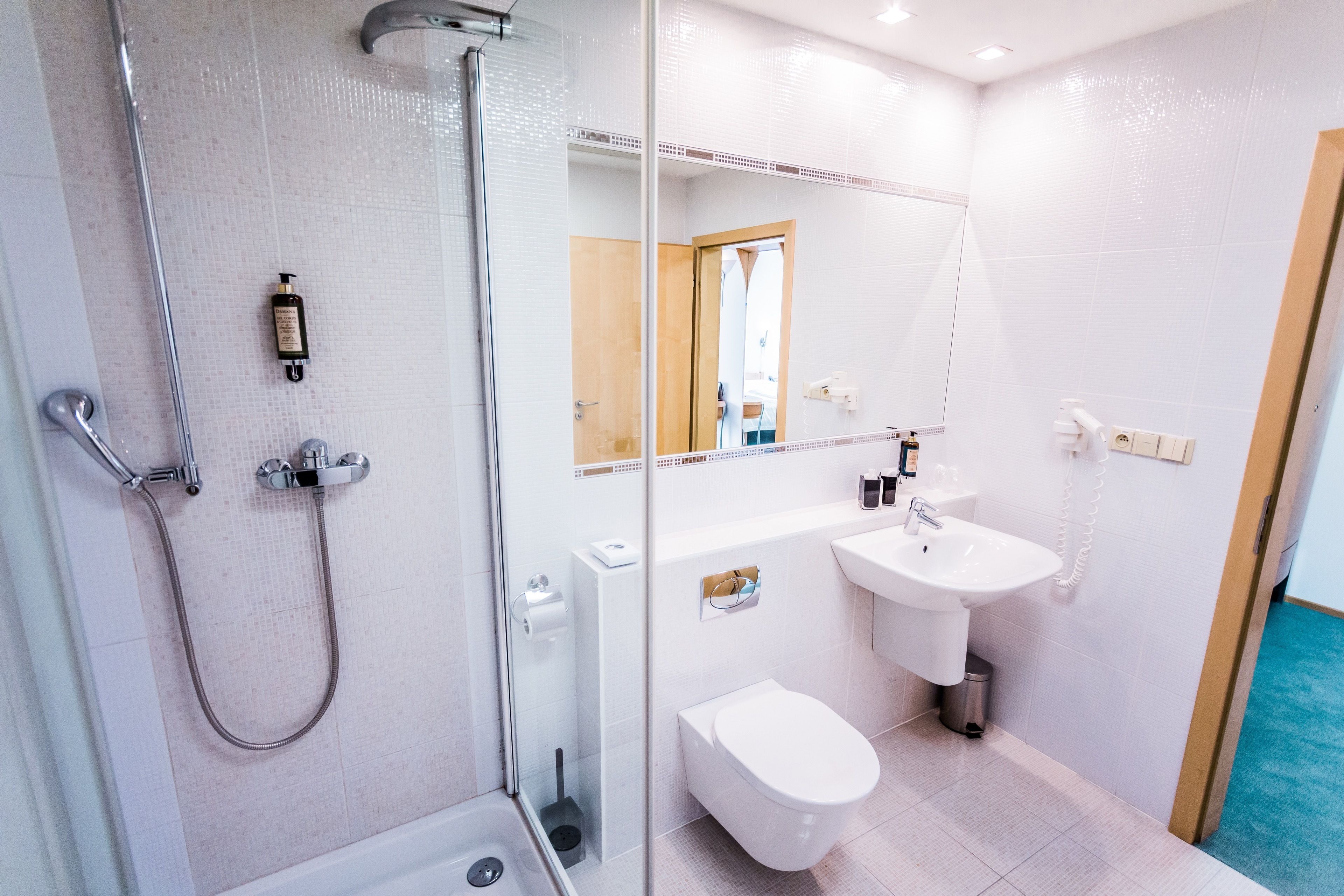 Un baño moderno con ducha de vidrio, inodoro blanco, lavamanos y espejo.