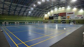An indoor sports hall with a blue floor, high ceiling, and multiple sports courts.