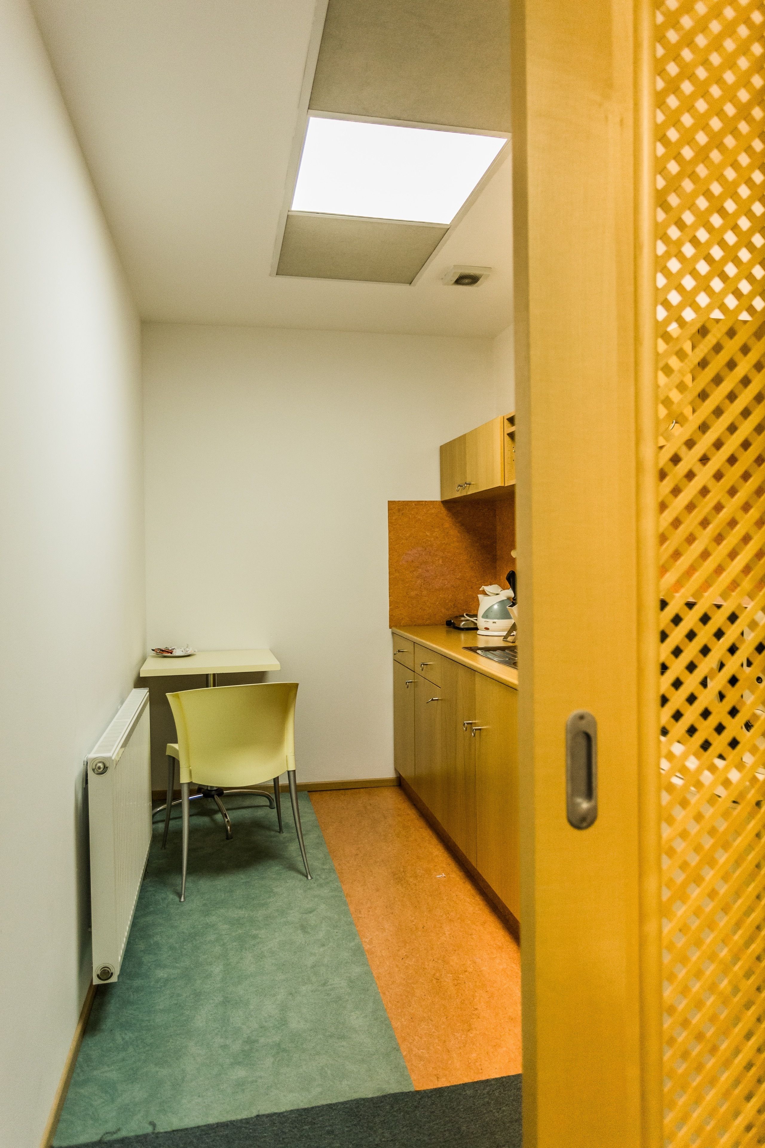 Un pasillo estrecho con kitchenette, un radiador, un escritorio y una silla.