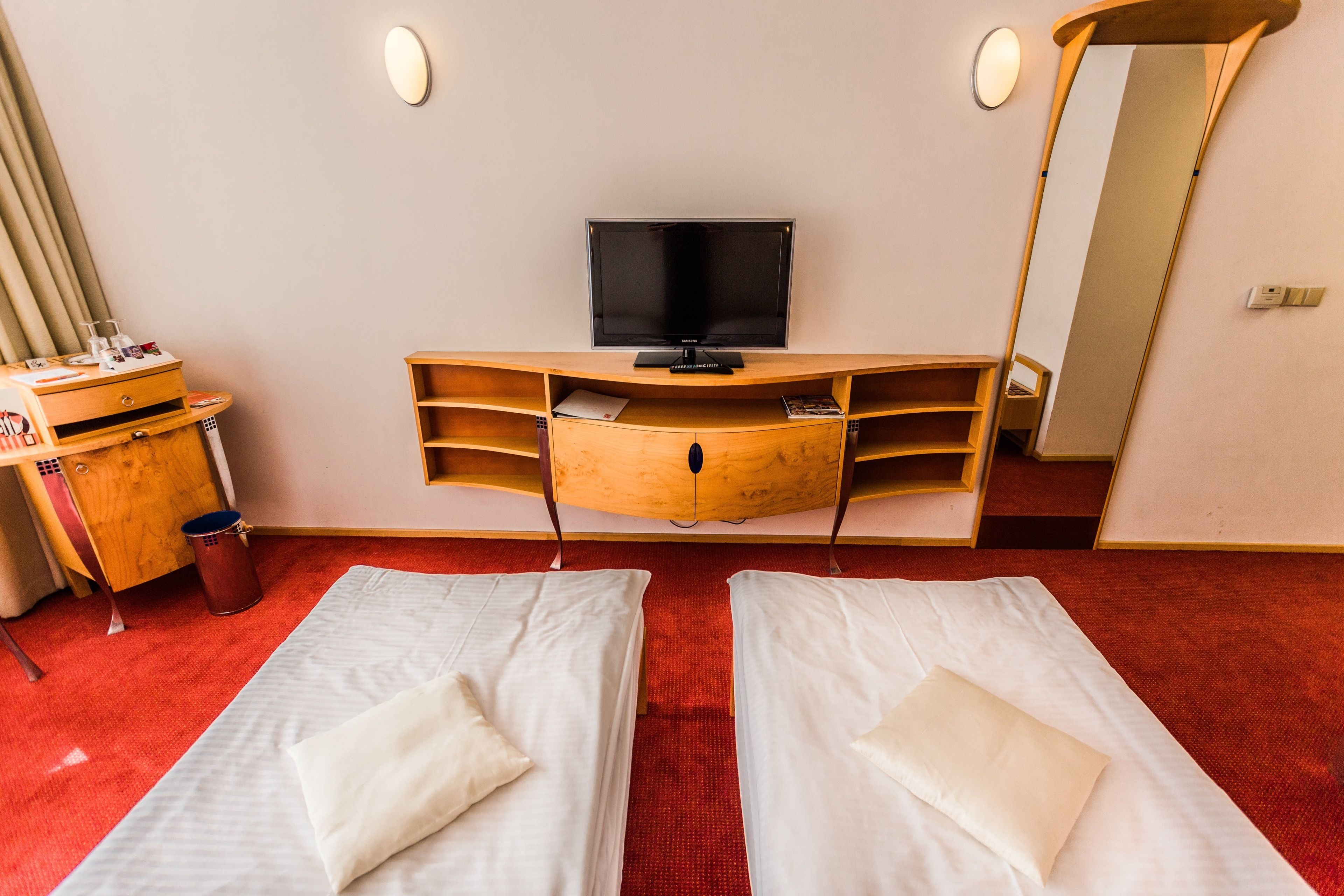 A hotel room with two beds, a TV, a wooden desk, and a mirror.