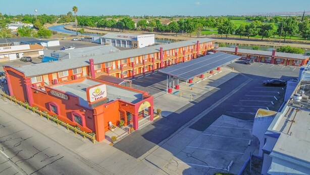 A motel with a red exterior, a parking lot, and a golf course in the background.