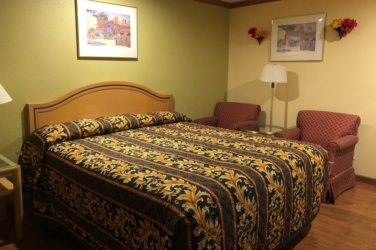 Une chambre d’hôtel avec un grand lit, une chaise, une lampe et deux tableaux encadrés au mur.