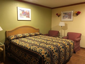 A hotel room with a large bed, a chair, a lamp, and two framed pictures on the wall. - Sun Star Inn Los Banos (Los Banos)