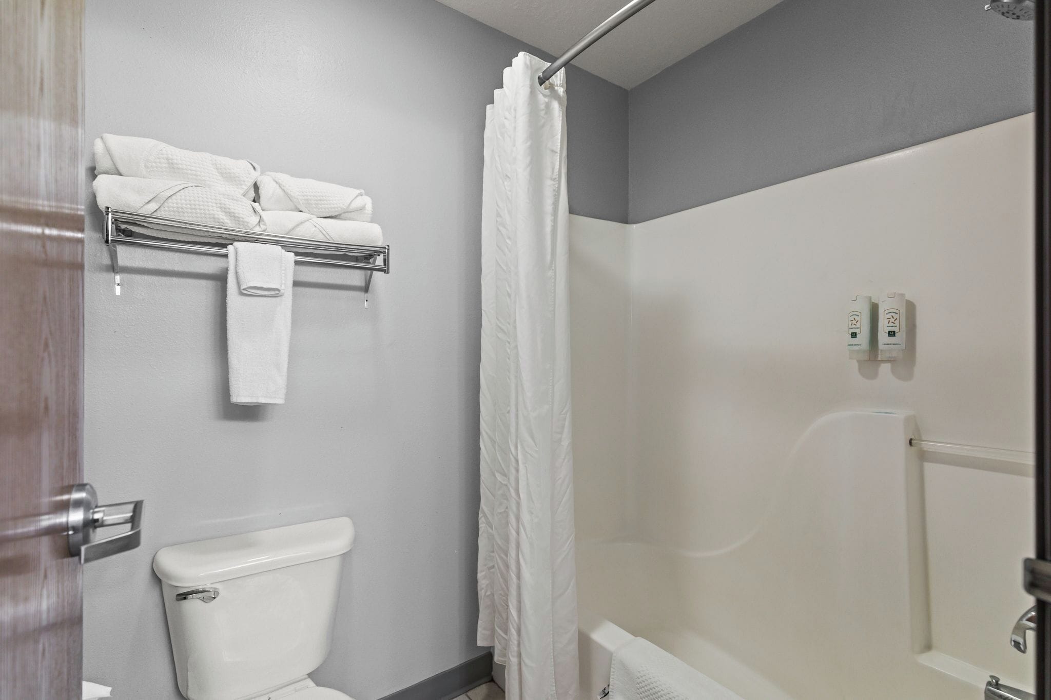 A bathroom with a toilet, a shower with a curtain, and a towel rack with folded towels.