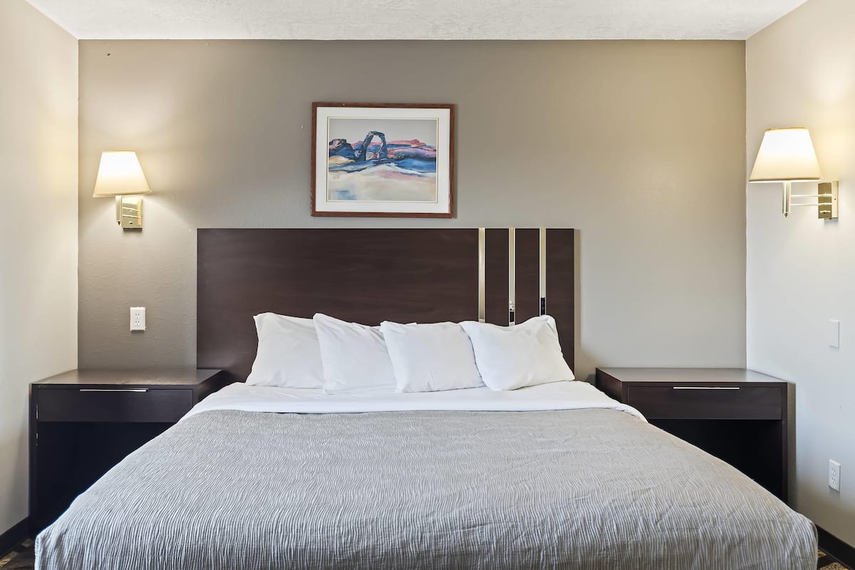 A hotel room with a large bed, two bedside tables, a framed painting on the wall, and wall-mounted lamps.