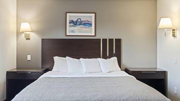 A hotel room with a large bed, two bedside tables, a framed painting on the wall, and wall-mounted lamps.