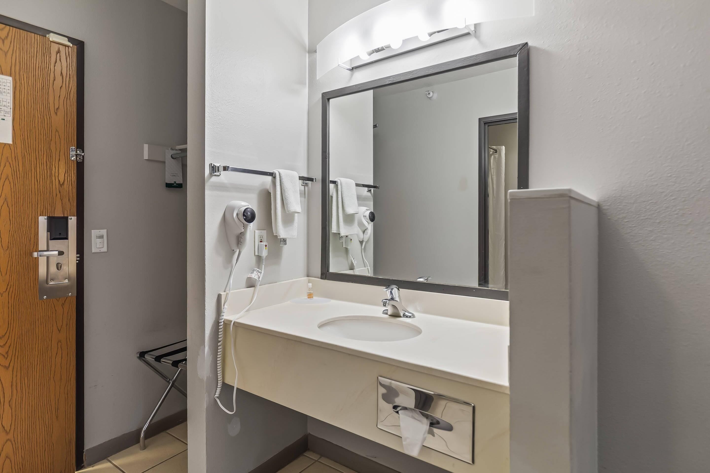 Un baño con lavamanos, espejo, toallero y una puerta con cerradura.