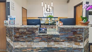 A reception desk with a stone facade, a 'Quality' sign, and a potted orchid.