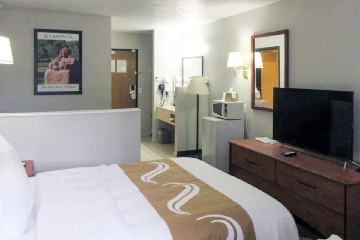 A hotel room with a bed, a TV, a desk, and a bathroom visible in the background.