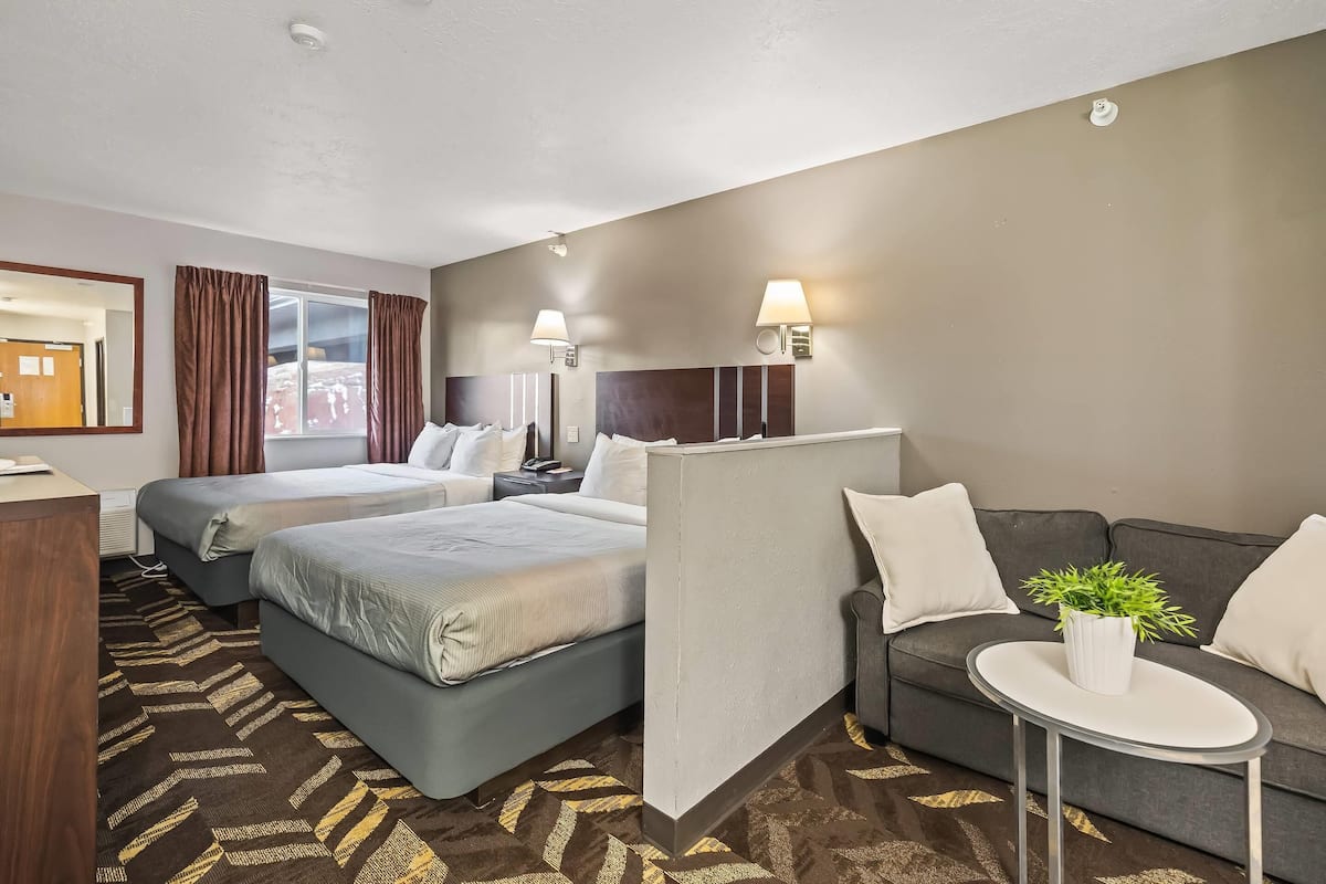 A hotel room with two beds, a sofa, a small table with a plant, and a window with curtains.