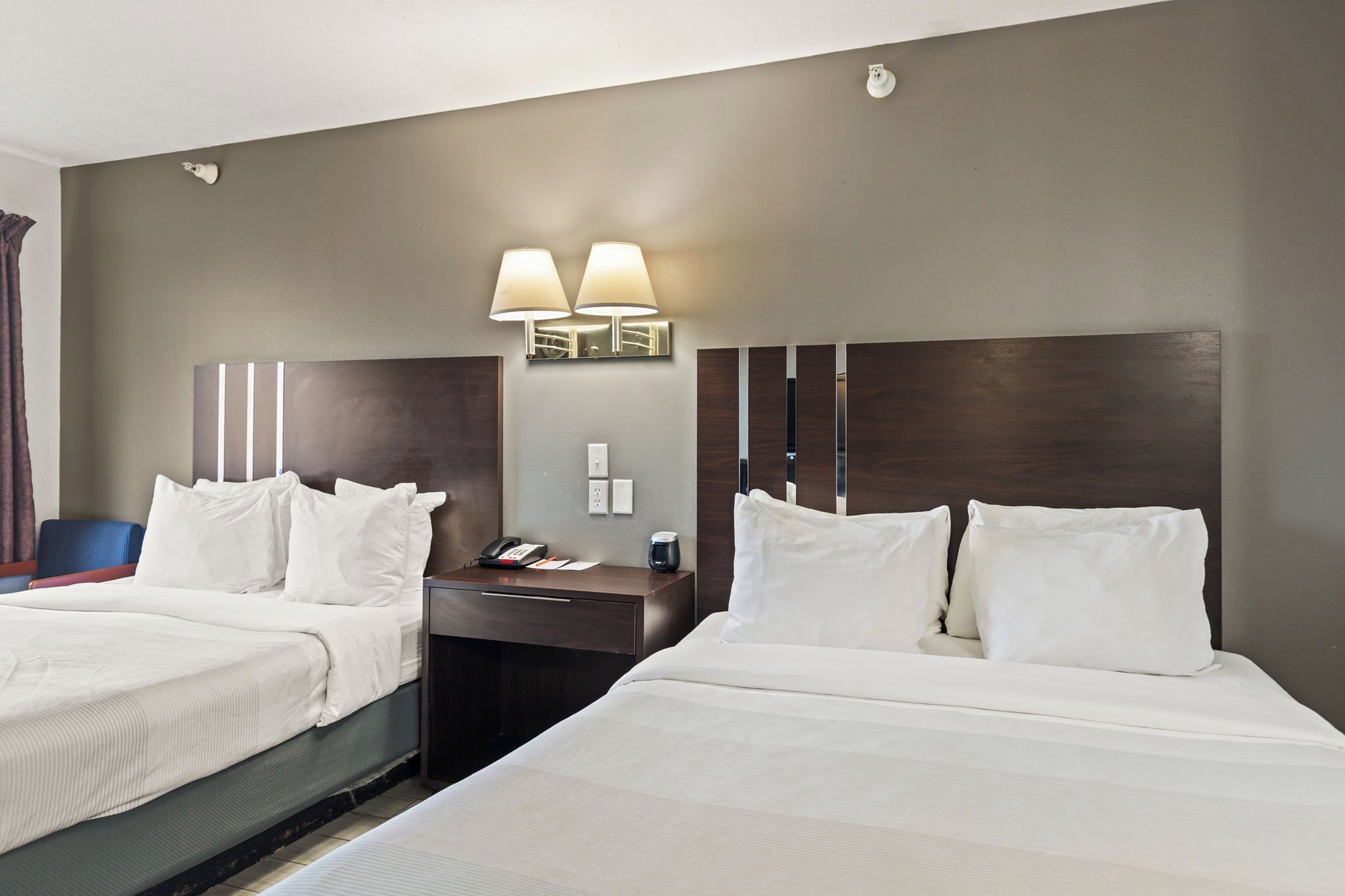 Une chambre d’hôtel avec deux lits, une table de chevet avec une lampe et un luminaire fixé au mur.