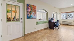 A breakfast room with a sign, a colorful painting, a desk with a computer, and a window with a view.