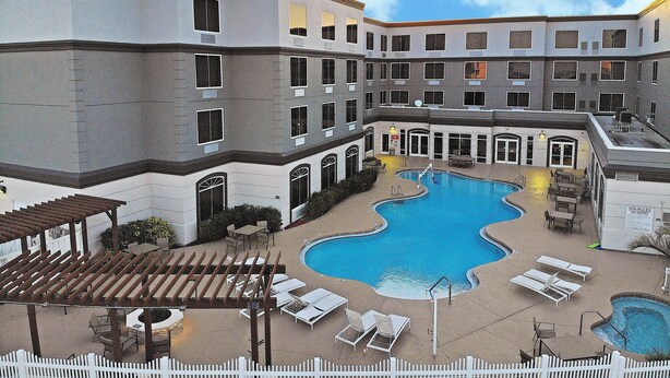 A hotel with a swimming pool, outdoor seating, and a white picket fence. - Country Inn & Suites by Radisson, Port Canaveral, FL (Cape Canaveral)