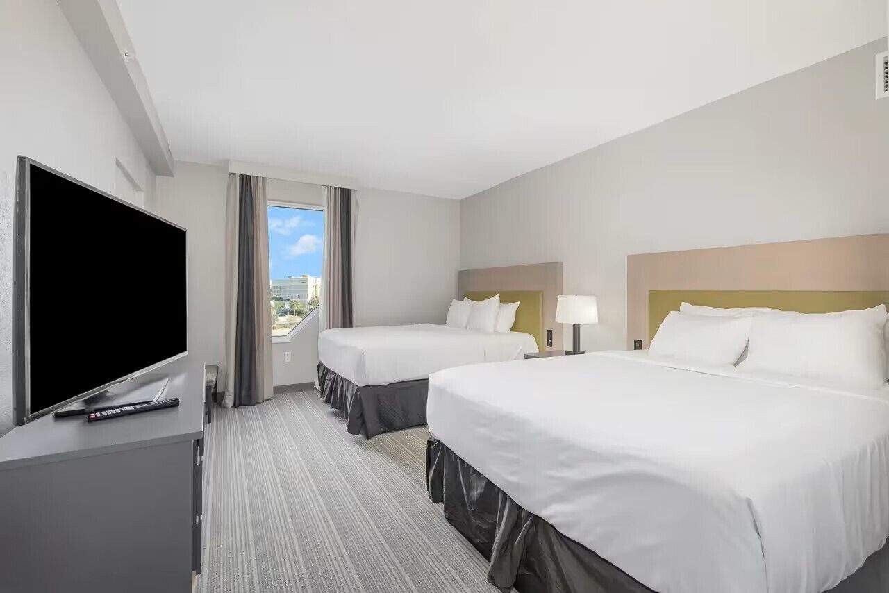 A hotel room with two beds, a TV, and a view of the city.