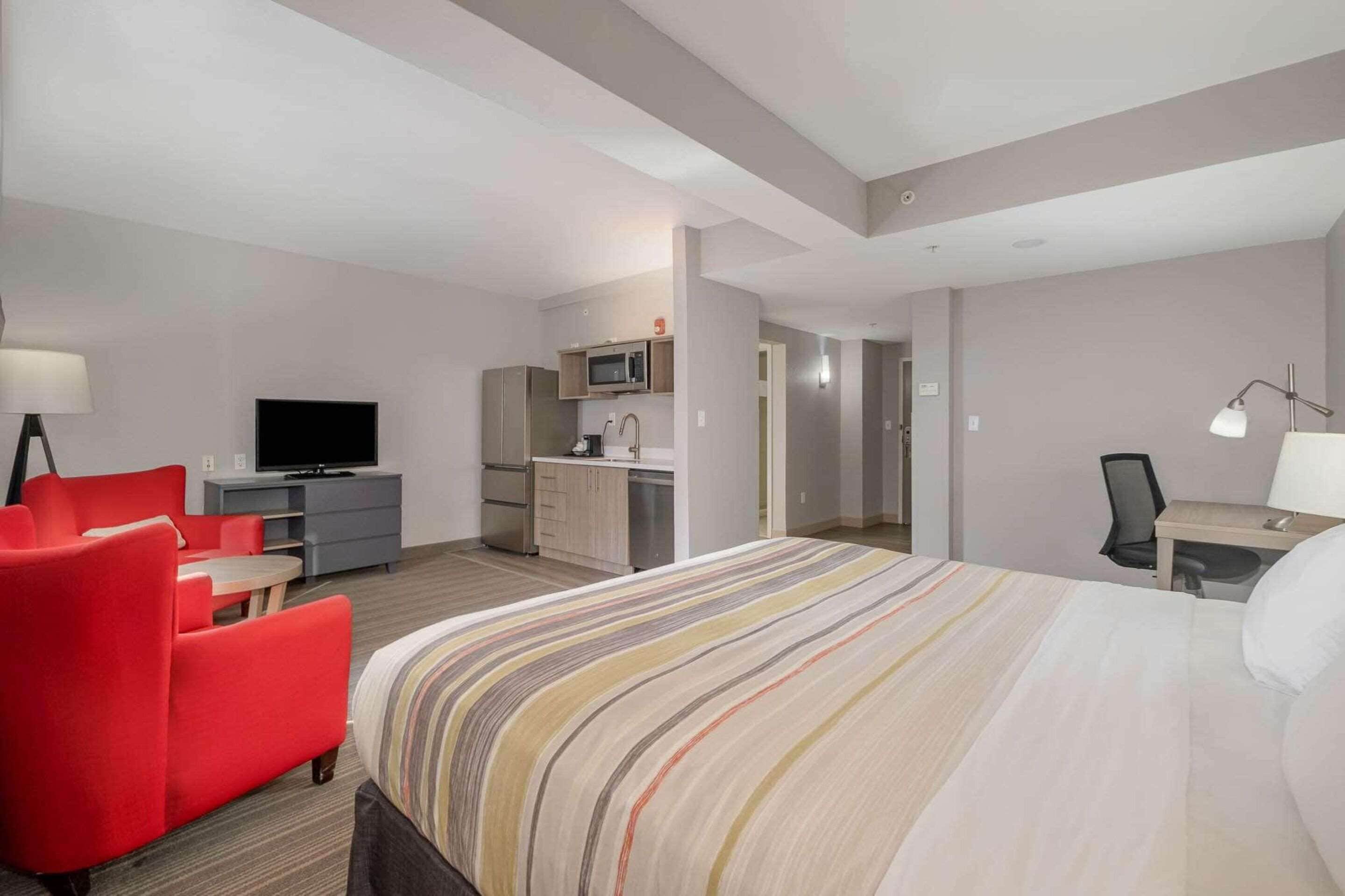 A hotel room with a bed, a desk, a red sofa, a TV, a microwave, and a small kitchen area.