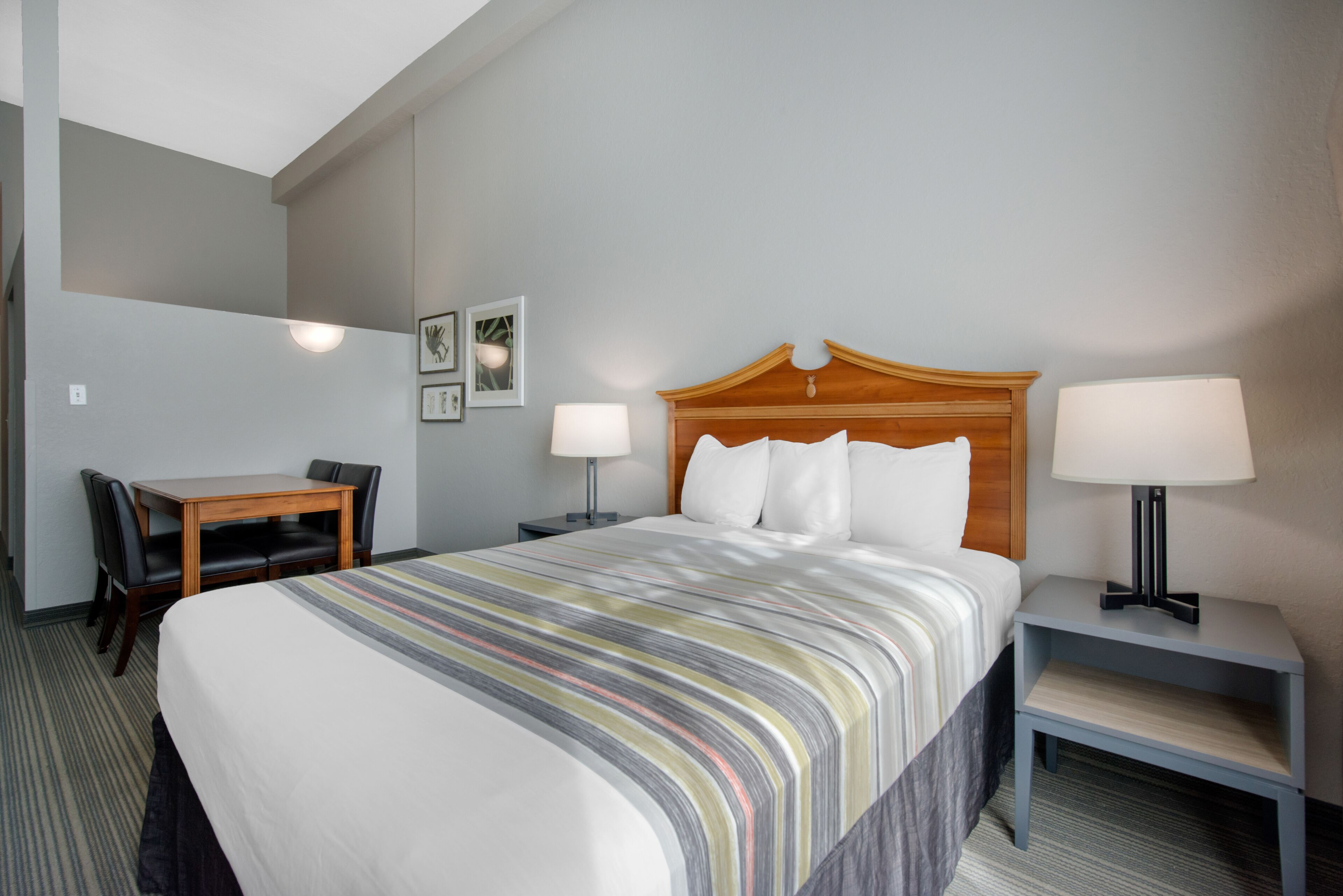 Quarto de hotel com cama, mesas de cabeceira, escrivaninha e cadeiras.