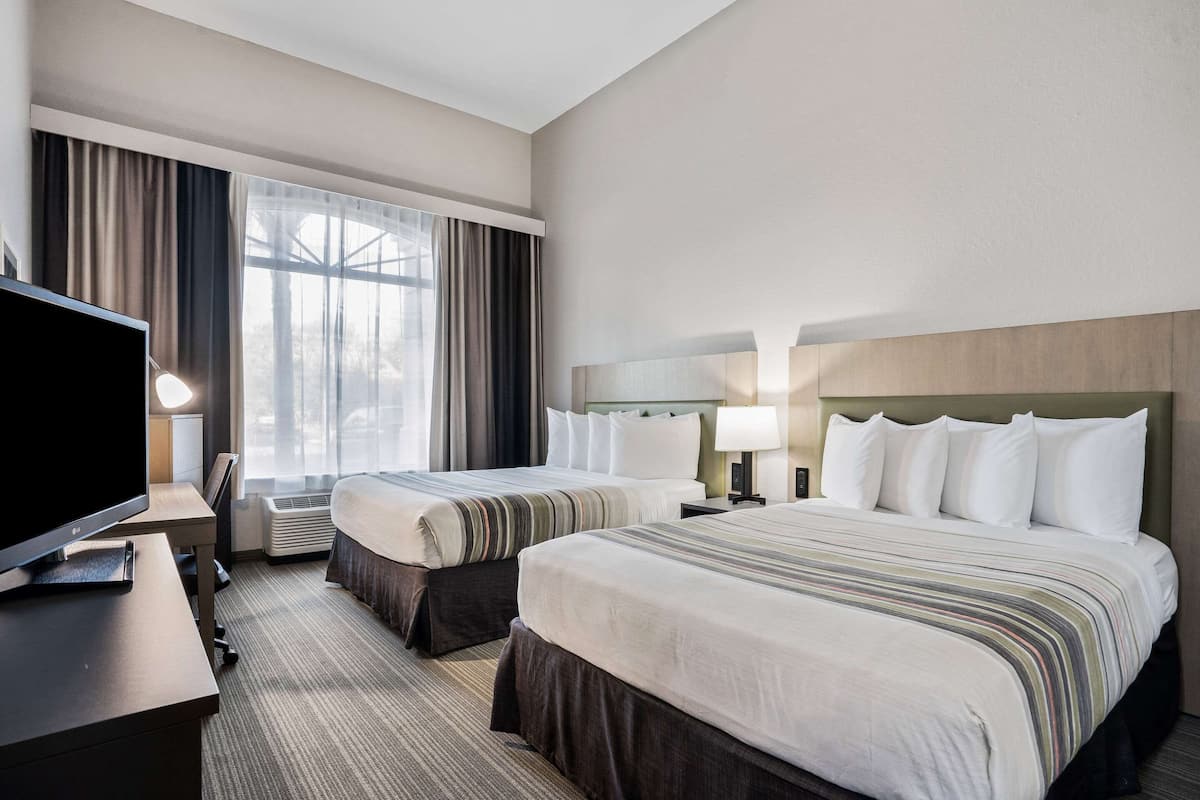 A hotel room with two beds, a desk with a television, and a large window with curtains.