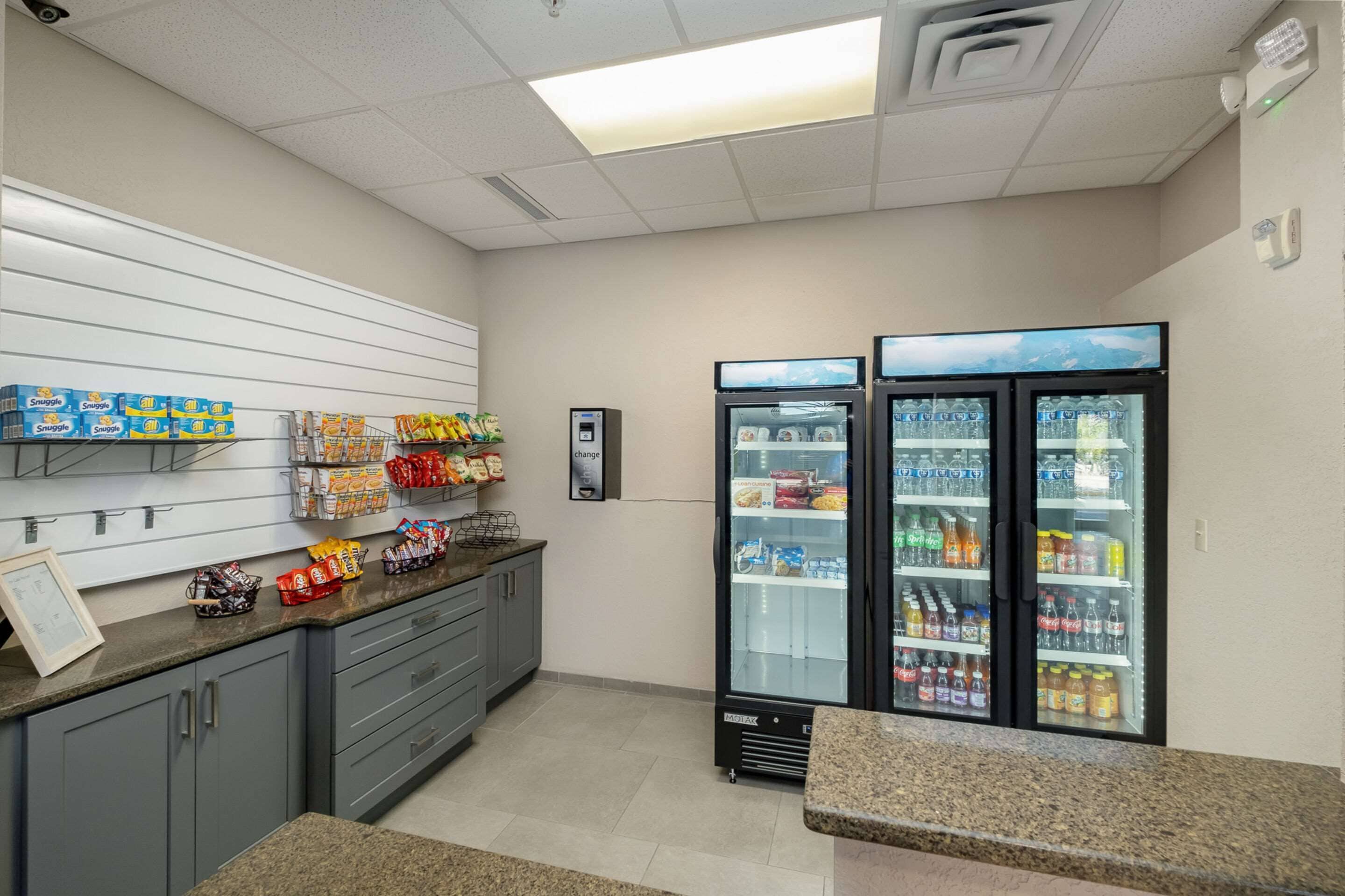 Una kitchenette equipada con microondas, refrigerador y estante lleno de bocadillos.