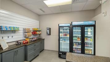 Una kitchenette equipada con microondas, refrigerador y estante lleno de bocadillos.
