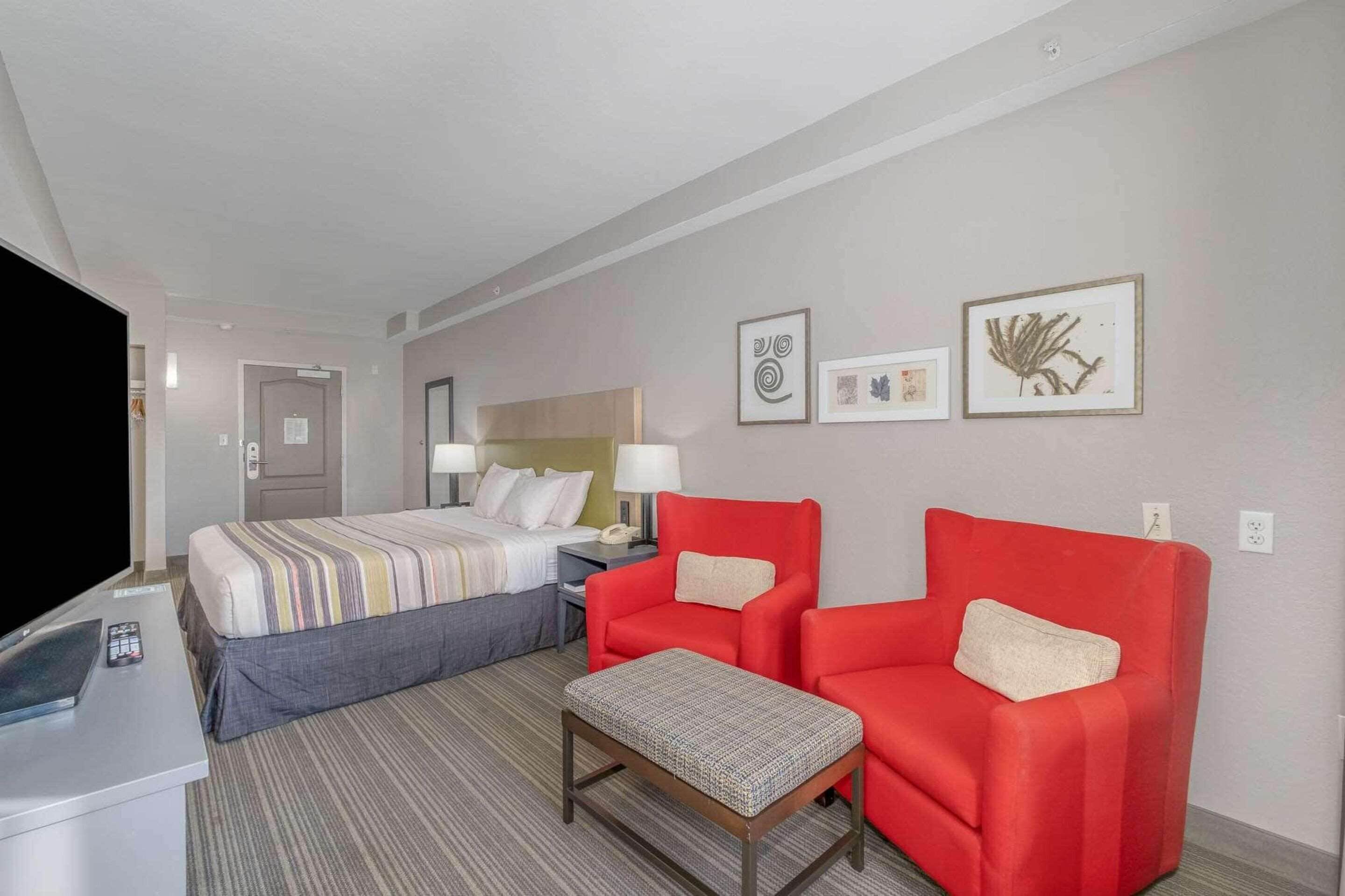 Ein Hotelzimmer mit einem Bett, zwei roten Sessel, einem kleinen Tisch, einem Fernseher und einem Schreibtisch mit Computer und Telefon.