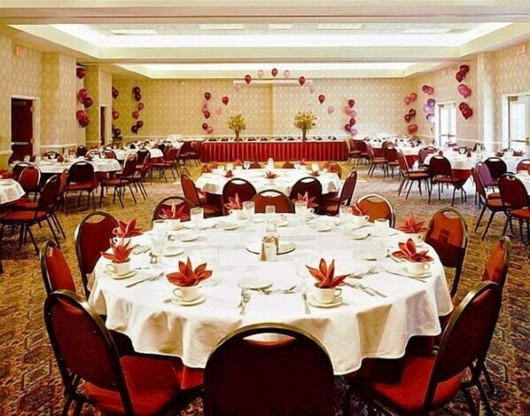 A banquet hall with round tables set for dining, red chairs, and a red carpeted floor.