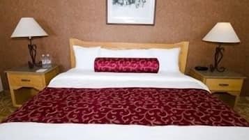 A hotel room with a bed, two nightstands, a red patterned bedspread, white pillows, and two lamps.