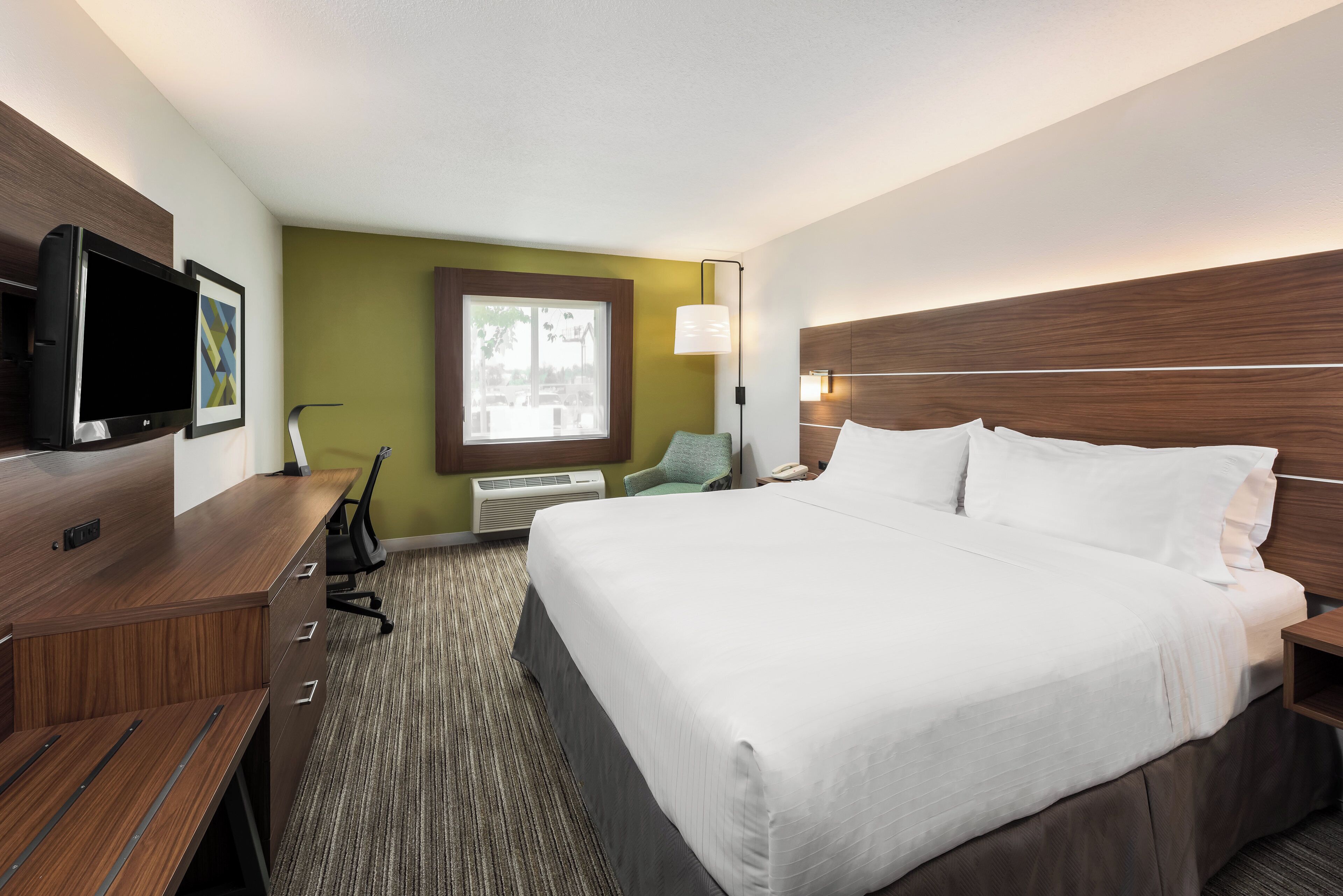 Hotelkamer met een groot bed, een bureau met een flatscreen-televisie, een stoel, een raam met uitzicht en een wandlamp.