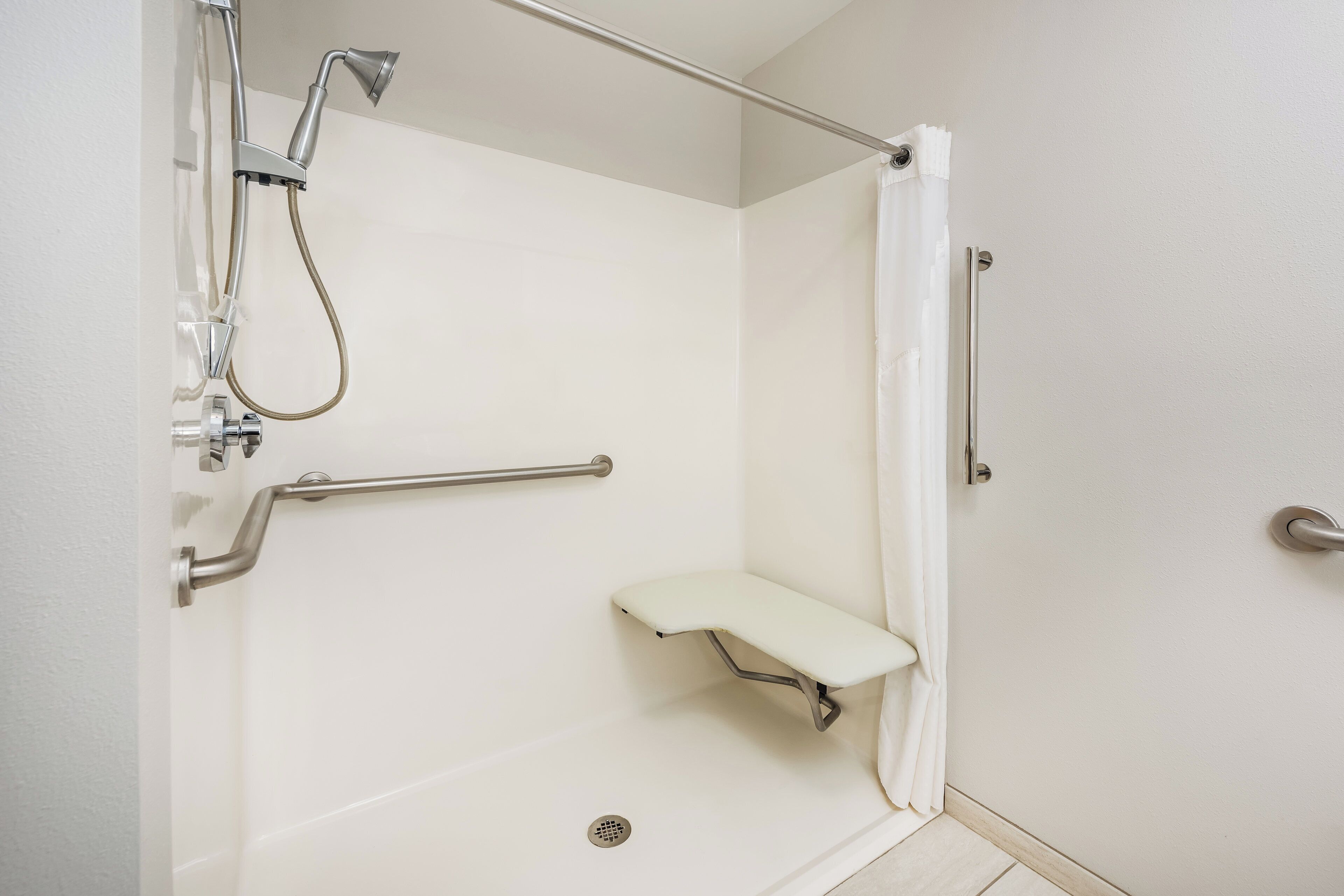Une douche équipée d’un pommeau de douche à main, d’une barre d’appui et d’un banc.