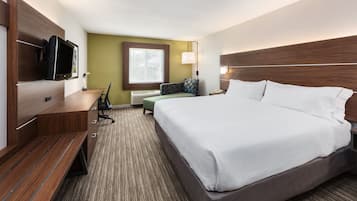 A hotel room with a large bed, a desk with a flat-screen TV, a chair, and a window with a view of trees.