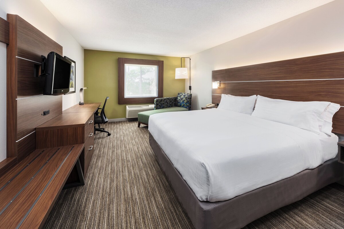 A hotel room with a bed, a desk, a television, a lamp, and a window.