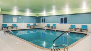 A pool area with clear blue water, metal pool ladders, and blue chairs arranged around the pool. - Holiday Inn Express Warrenton by IHG (Warrenton)