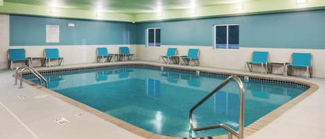 Un área de piscina con agua azul cristalina, escaleras de metal y sillas azules dispuestas alrededor.