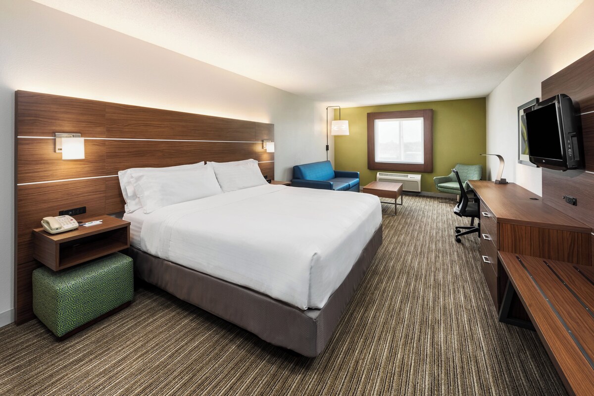 A hotel room with a bed, a desk, a chair, a television, and a window.