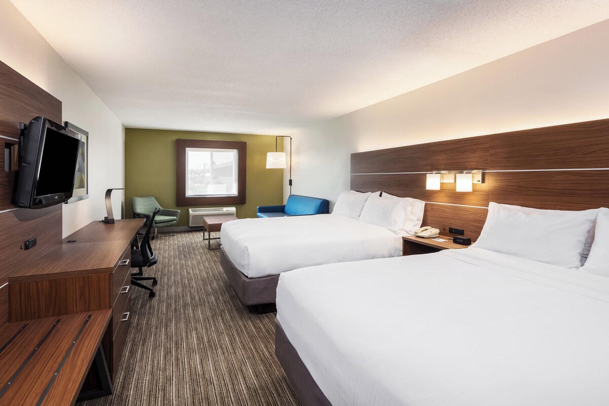 A hotel room with two beds, a desk, a television, a chair, and a window.